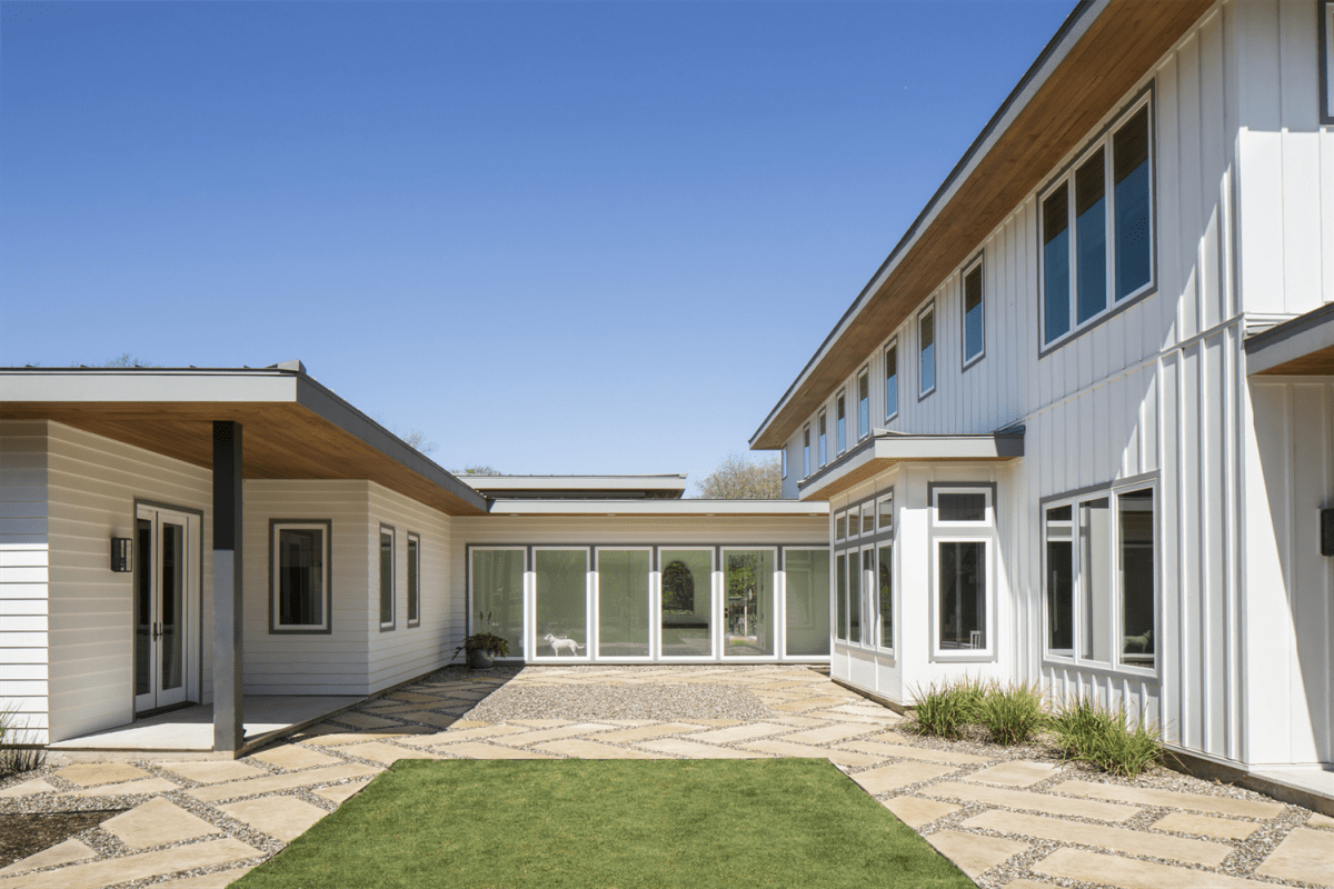 A home with white board & batten siding and a glass breezeway. In the breezeway is a white dog.