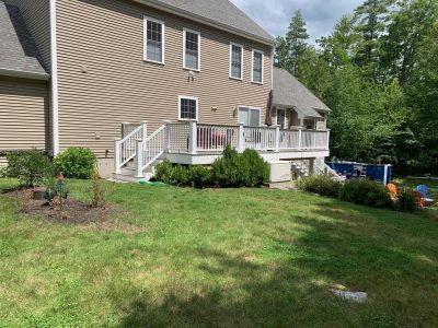 A pressure treated wood deck with white railings on the backside of a tan home in Strafford, NH.