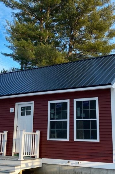 A red home with new black metal roofing with 2 ladders leaning on the side of the home.