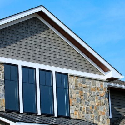 A home with gray clapboard and Beach House Shake siding, stone accenting, and white trim.