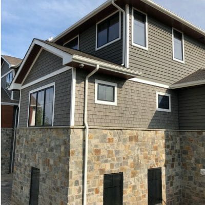 A home with gray Beach House Shake and clapboard siding on its top half and stone work on the bottom.