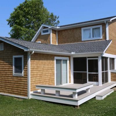 A home with tan Beach House Shake siding, white trim, and a beige and white composite deck attached to a screened porch.