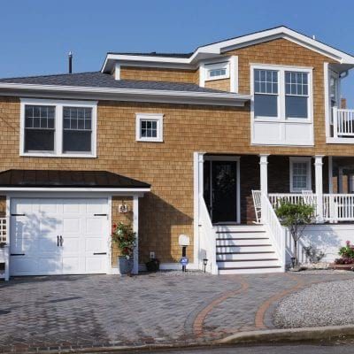 A 2 story home with tan Beach House Shake siding, white trim, railings, stairs, and garage door.