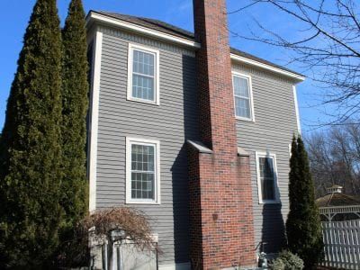 A 2 story home in Hampton, NH with tan clapboard siding and a large brick fireplace and chimney.