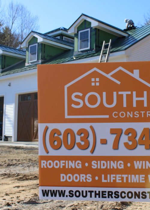 A Southers Construction sign placed in front of a home with workers installing a new green metal roof in Danville, NH.