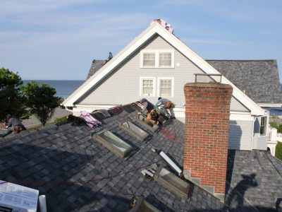 Roofers replacing a shingled roof on a home in Rye, NH.