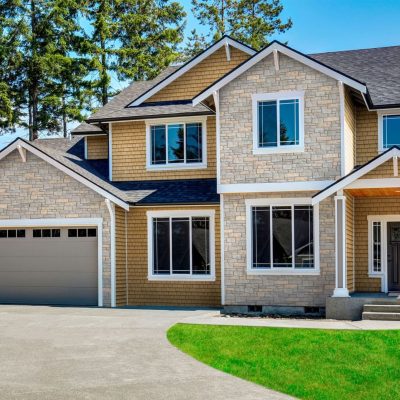 A 2 story home with tan Tando shake siding and stone accents around the garage and front windows.