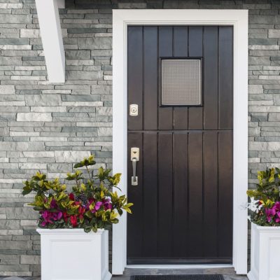 A dark brown wooden entry door surrounded by gray TandoStone siding.