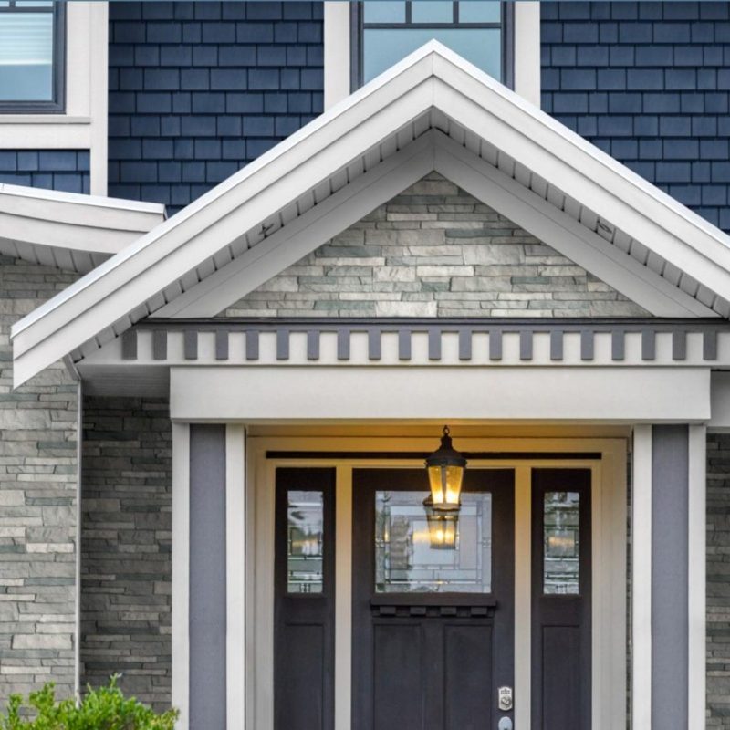 The entry way of a home with a dark brown door surrounded by gray TandoStone and blue TandoShake siding.