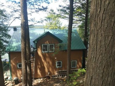 A man on a ladder working on a home with a green metal roof.