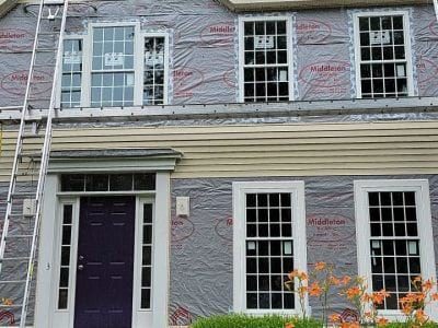 A home covered in plastic underlayment before its new siding is applied.