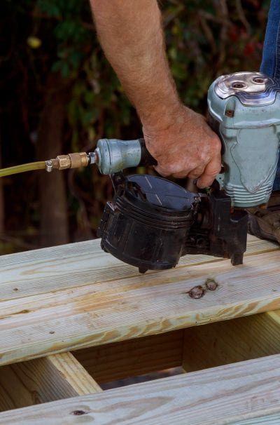 A man using a nail gun to build a deck with pressure treated wood.