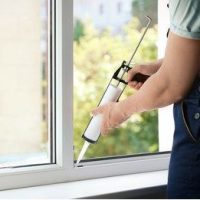 A person applying caulking to the interior of a window.