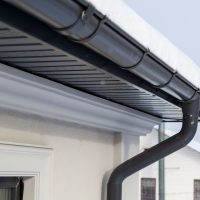 Corner of the house with new gray metal tile roof and rain gutter at winter. Metallic Guttering System, Guttering and Drainage Pipe Exterior