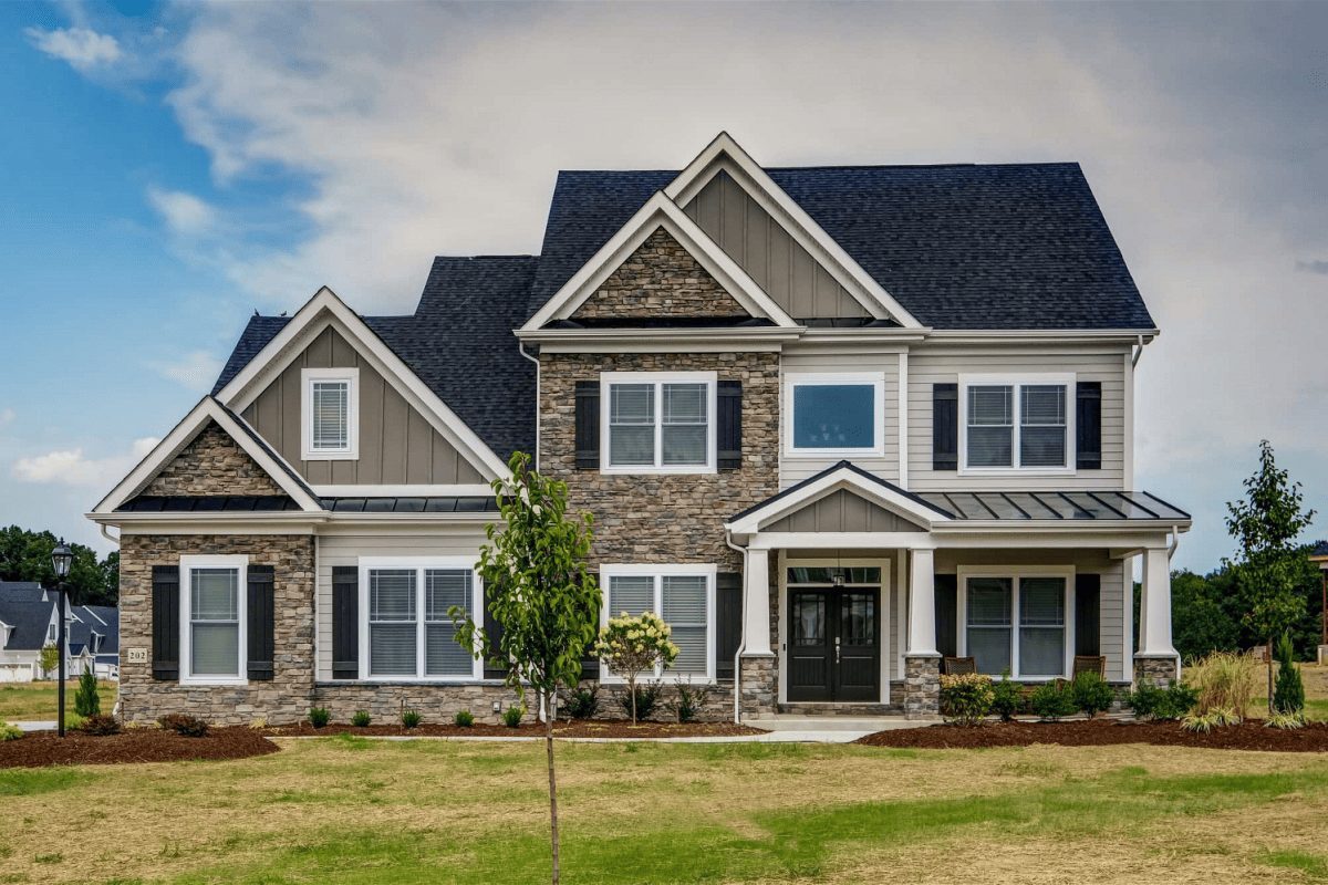 A large 2 story home with tan board & batten siding and stone siding accents.