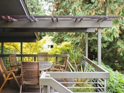 A wood deck with white railings surrounded by trees with a wooden table and 6 chairs.