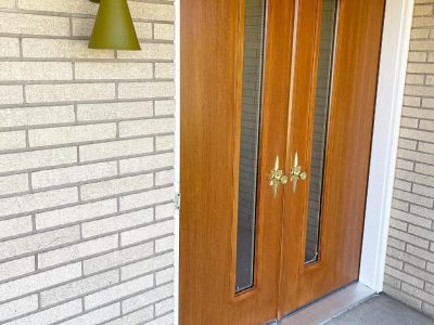 Double hinged wood doors with thin full length windows on a brick home with white trim.