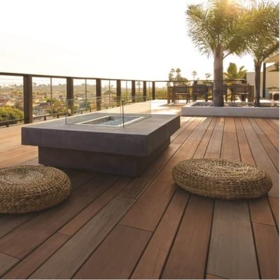 A mahogany composite deck with a glass fireplace and 2 floor cushions next to it. The deck has brown composite railings.